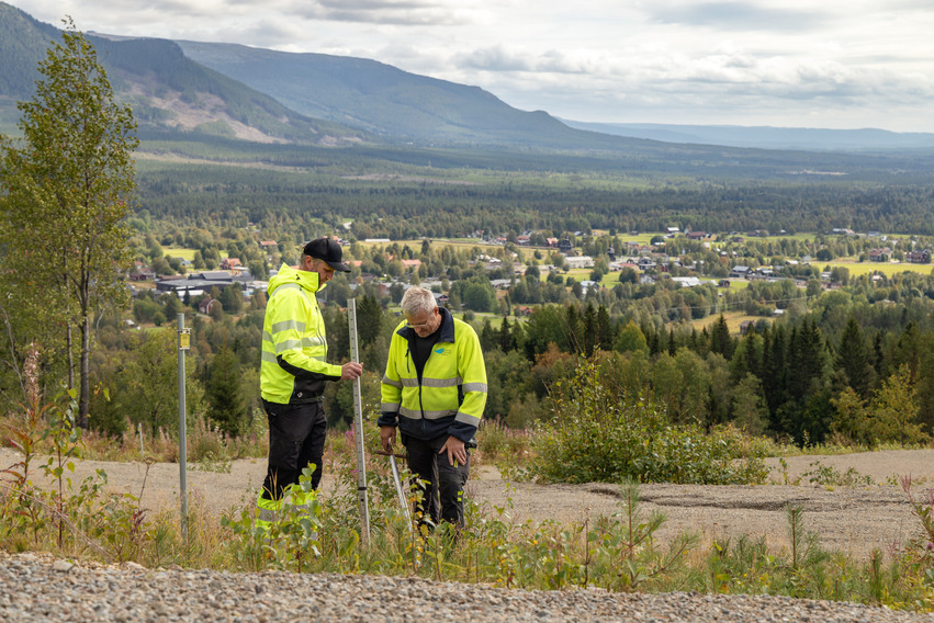 Två personer för markmätning med fjäll i bakrunden