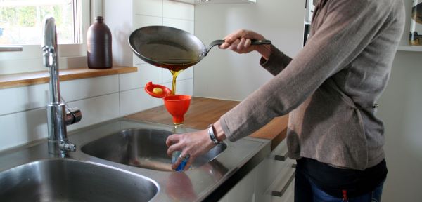 Här står en person och häller överblivet matfett i en flaska genom att använda en miljötratt.